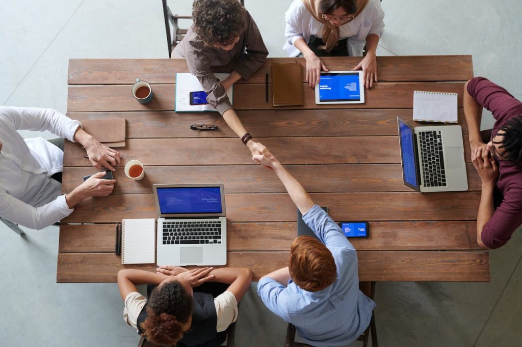 group-of-person-sitting-indoors-3184306 Overhead view of colleagues in a work meeting using laptops and tablets, emphasizing teamwork and technology.